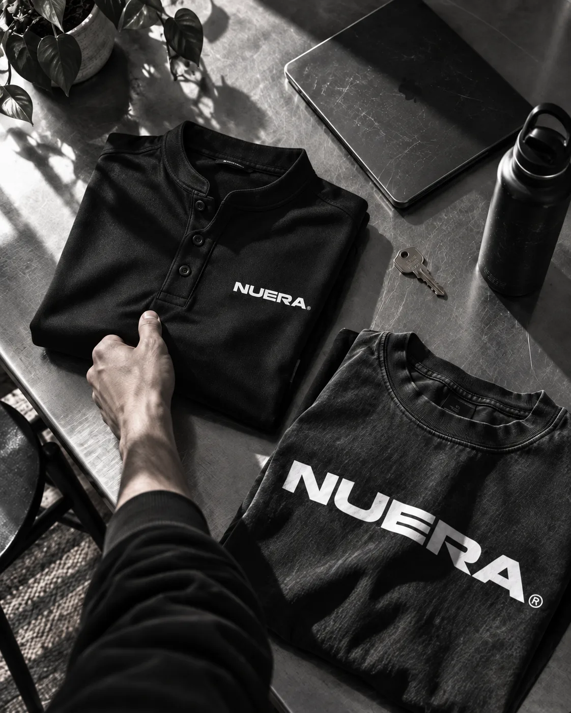 A NUERA collarless field polo and oversized tee laid out with a tablet and keys.