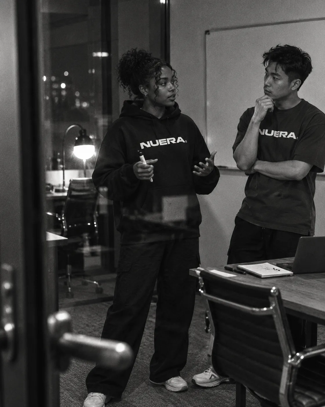 Two adults practicing a conversation in NUERA clothing, seen through a glass door.