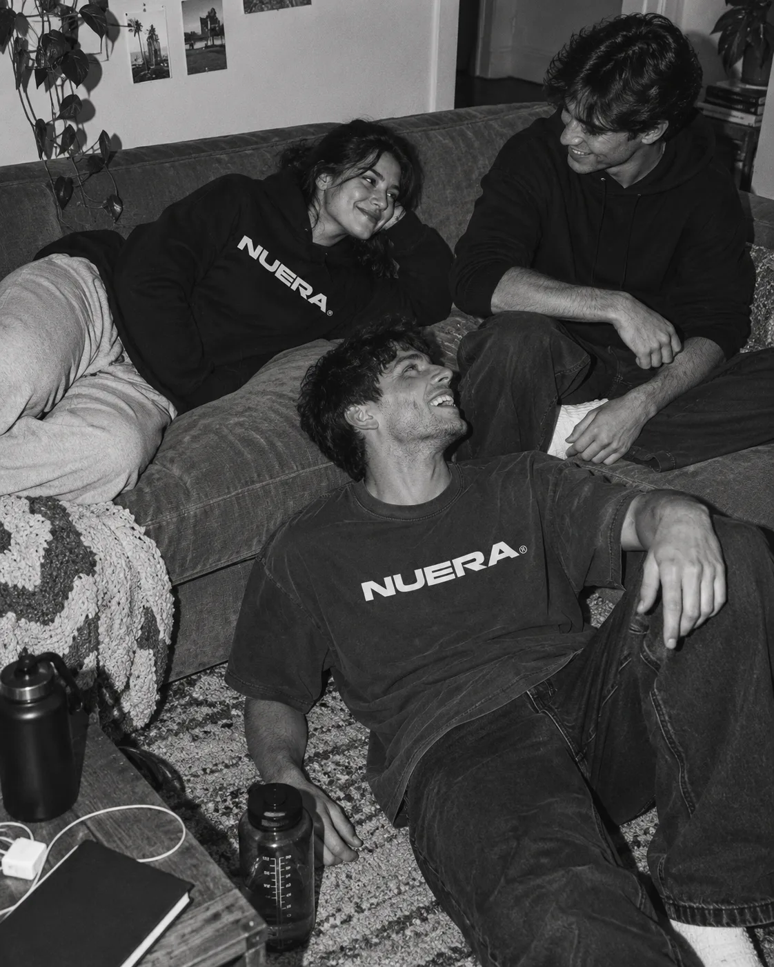 Three friends relaxing on and beside a sofa in NUERA oversized tees and hoodies.