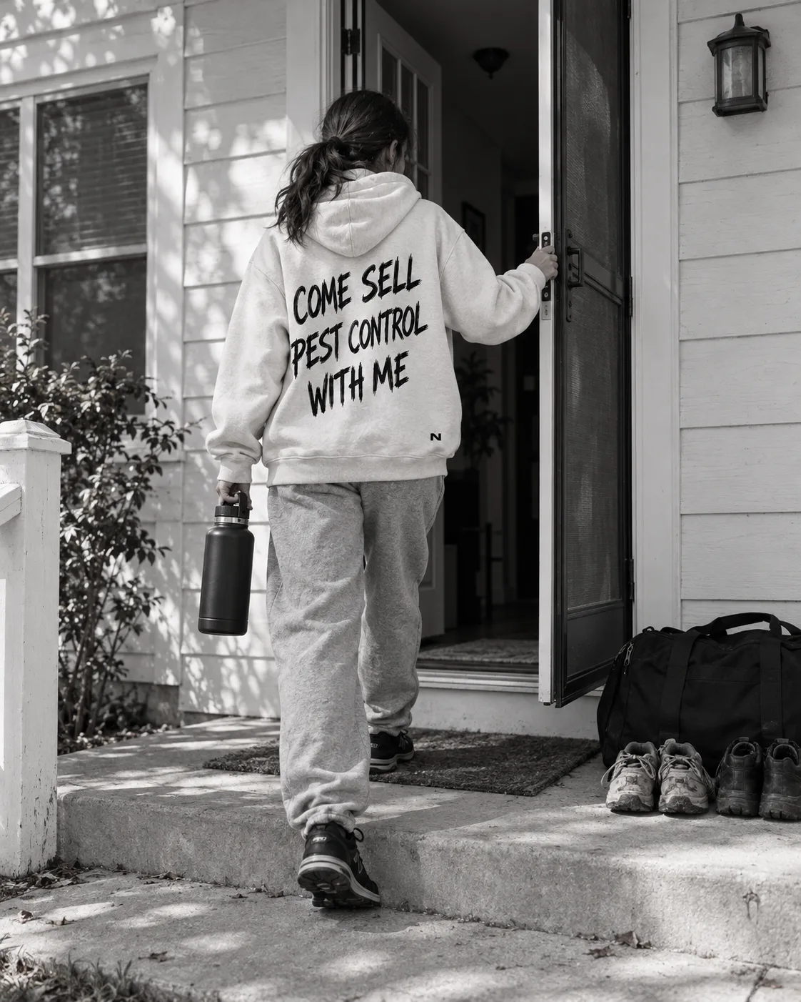 A person in a white Come Sell Pest Control With Me hoodie opening the door of the shared house.